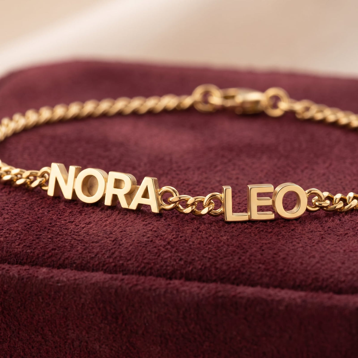 Close-up of gold name bracelet showing the NORA and LEO name pieces, curb chain and clasp