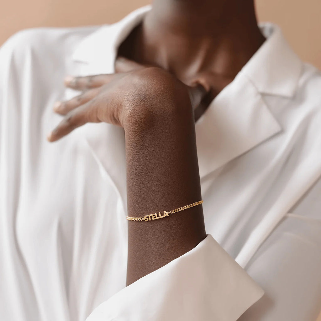Personalised gold-tone name bracelet worn with a white blazer